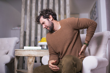 Obraz premium unhappy Man suffering from backache at home. Lower Back Pain . Man feels back pain massaging aching muscles, sad man suffers from low-back
