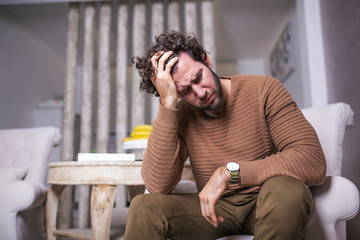 Portrait of an handsome man sitting on a sofa at home with a headache, feeling pain and with an...