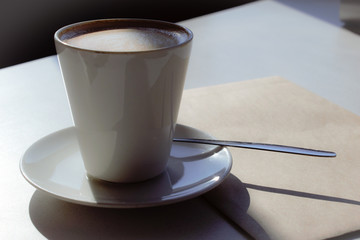 Cup of coffee  with saucer and spoon and brown envelope