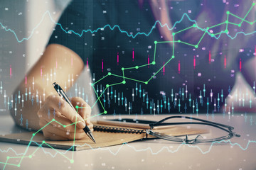 Multi exposure of woman's hands making notes with forex graph hologram. Concept of technical analysis.