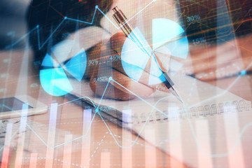A woman hands writing information about stock market in notepad. Forex chart holograms in front. Concept of research. Multi exposure