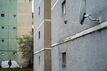 Satellite antenna mounted on a block of flats wall and a distant person walking by a white cover in a dreary residential compound.