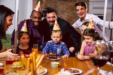 Fototapeta na wymiar Portrait of happy multiethnic family celebrating a birthday at home. Big family eating cake and drinking wine while greeting and having fun children. Celebration, family, party, home concept.