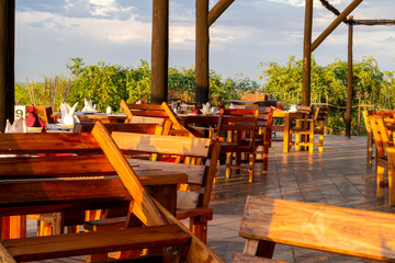 Wooden chairs placed against te tables on an outside terrace in nature, ready to receive guests