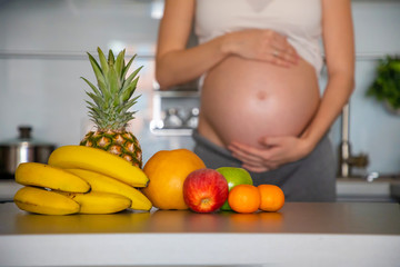 Obraz na płótnie Canvas Pregnant woman and different tropical fruits in home kitchen