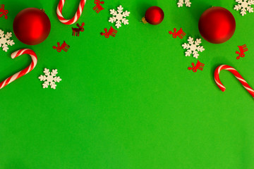 Flat lay Christmas composition with candy canes and ornaments on green background