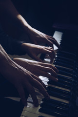 playing four male hands on the piano. palms lie on the keys and play the keyboard instrument in a music school. student learns to play. hands of a pianist. black dark background. © Yuliia