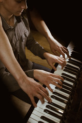 playing four male hands on the piano. palms lie on the keys and play the keyboard instrument in a music school. student learns to play. hands of a pianist. black dark background.