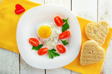 A plate of tomatoes, fried egg and heart shaped bread. Festive romantic food.