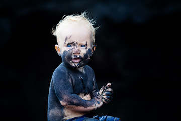 Funny portrait of happy smiling child with dirty face, hands playing with fun on black sand beach in sea water pool before swimming. Family lifestyle active leisure on summer vacation with little baby