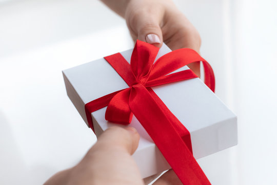 Gift Present Box With A Red Ribbon Bow Isolated On A Bright White Background. Passing Present For A Valentine's Day From Hand To Hands. Love And Holiday Concept.