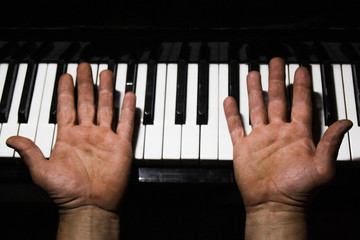 four male hands on the piano. palms turned upside down on a keyboard in a music school. student learns to play. hands of a pianist. black dark background.