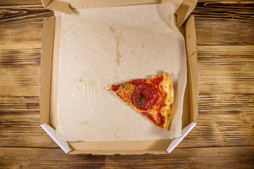 Last slice of pizza in cardboard box on a wooden table. Top view. Concept for home delivery of food, fast food, delivery of pizza