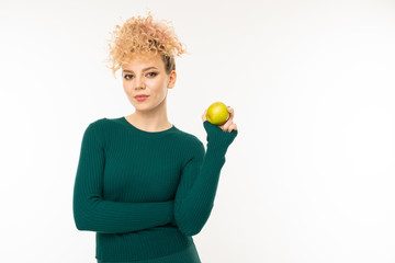 european curly blond girl with a good figure holds an apple in his hand on a white wall