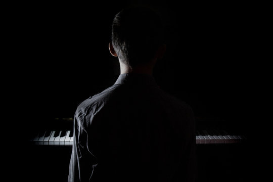 Silhouette of a young man sitting at the piano. The boy emotionally plays the keyboard in a music school. student learns to play. hands of a pianist. black and white photography.