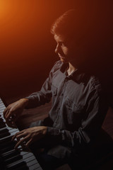 Fototapeta na wymiar young man sitting at the piano. boy emotionally plays the keyboard instrument in the music school. student learns to play. hands pianist. black dark background. vertical.