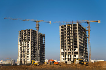 Fototapeta na wymiar Tower cranes constructing a new residential building at a construction site against blue sky. A group of excavators digs a pit for the construction of the foundation of a building.