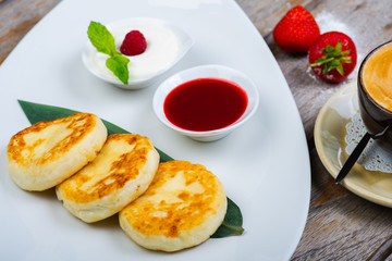 Traditional breakfast with coffee and cheesecakes, cottage cheese pancakes on a plate with syrup and jam.