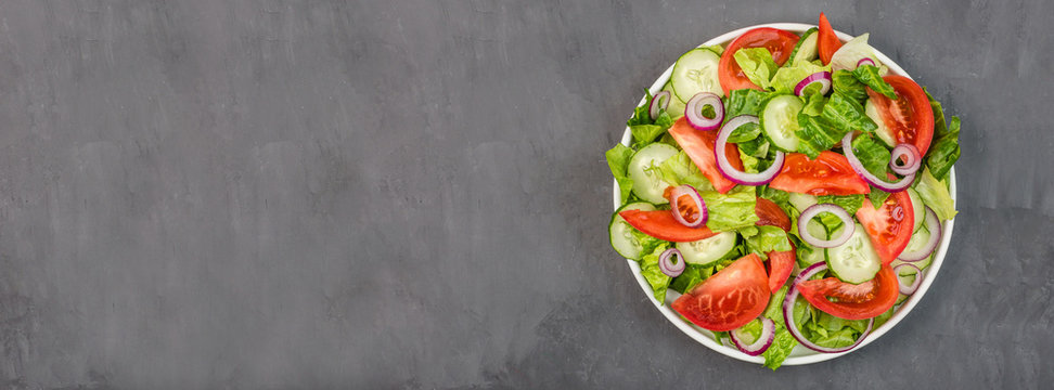 Healthy vegetarian dish on table, vegetable salad with fresh tomato, cucumber, lettuce, red onion on gray concrete background. Diet menu. Top view. Flat lay, mockup, template with copy space