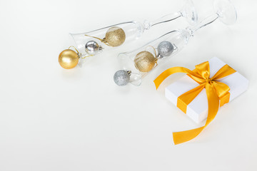 Paper gift box wrapped with yellow ribbon and champagne glasses filled with Christmas decorations, isolated on white background. Presents and holidays concept.