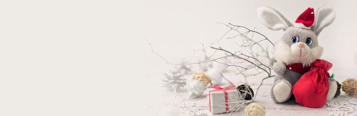 Christmas light gray background on whitewashed wooden boards with a toy hare in a Santa Claus costume with gifts