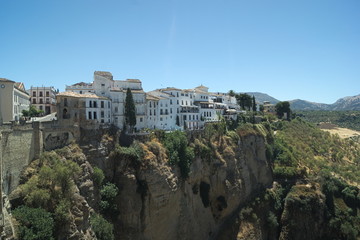 Naklejka premium View of the old city of Ronda in Spain. High above the river bed of the Tajo, elegant houses are perched on the top of the sheer rockface of the canyon.