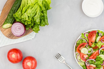 Healthy vegetarian dish on table, vegetable salad with fresh tomato, cucumber, lettuce, red onion on gray concrete background. Diet menu. Top view. Flat lay, mockup, template with copy space