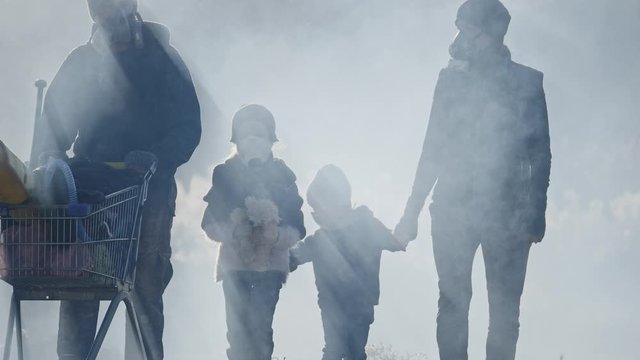 Survivor family in gas mask going through clouds of toxic smoke in desolate and burned out forest landscape.