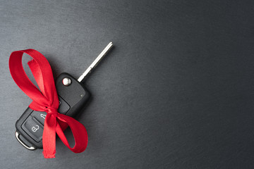 Car key with red bow on dark black slate plate background. Christmas or Valentine's Day gift or present abstract concept. Copy space on the right. Flat lay top view.