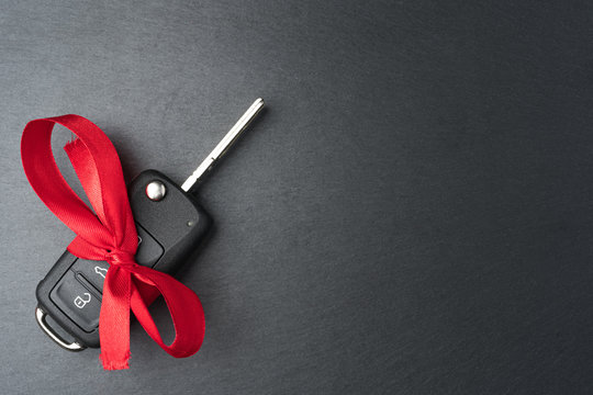 Car key with red bow on dark black slate plate background. Christmas or Valentine's Day gift or present abstract concept. Copy space on the right. Flat lay top view.