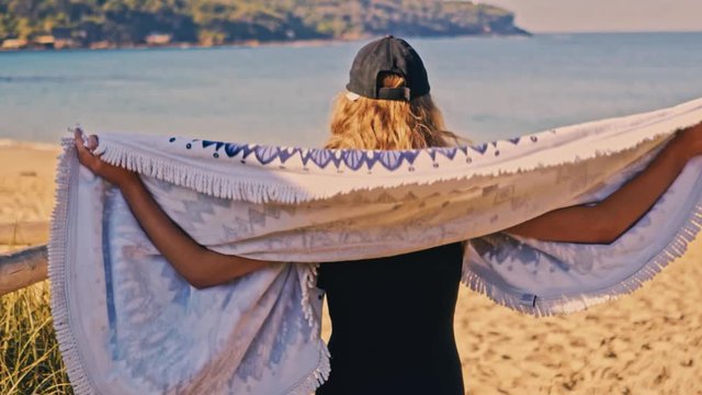 Young blond woman wearing cap and pareo fabric at beach, Slow motion