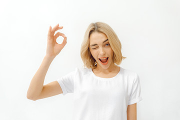 girl shows different emotions. woman in a white t-shirt on a white background shows the sign ok. copy space