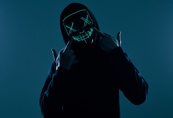 Anonymous man in black hoodie hiding his face behind a neon mask