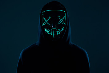 Anonymous man in black hoodie hiding his face behind a neon mask