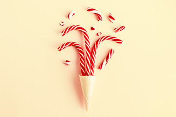 Fototapeta premium Creative Christmas still life with sweets, top view. Three Christmas canes and pieces of candy in a waffle cone for ice cream on a pastel pink background, close up. Winter holidays concept, minimalism