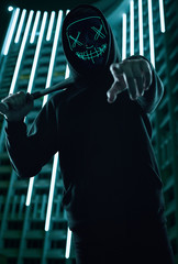 Anonymous criminal man with baseball bat in a black hoodie and neon mask
