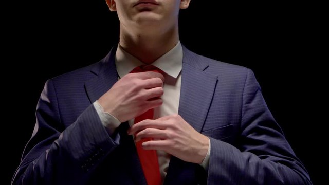 A young man in a simple blue suit and white shirt neatly straightens his red tie hands