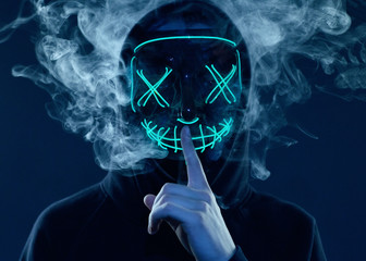 Anonymous man hiding his face behind neon mask in a colored smoke