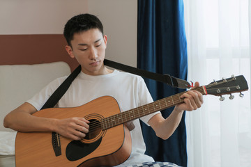 Obraz premium Asian man play guitar at home, feel relaxing