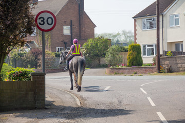 Riding road safety-young woman rides her horse through a village wearing correct safety gear an...