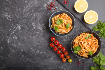 Semolina pasta with tomato pesto sauce, orange and herbs on a black concrete background.  Top view, copy space.