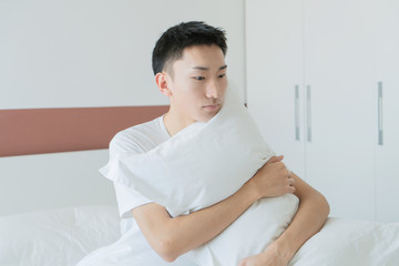 Obraz na płótnie Canvas asian young man holding pillow in bedroom in the morning