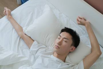 a young man waking up in bed and stretching his arms