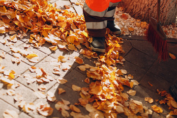 Janitor cleaner sweeping autumn leaves on the street