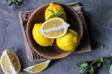 Photo of fresh ripe lemons on retro background. A slice of lemon with green leaves. Lemon fruit on wooden plate bowl. Top view. Copy space. Grey background. Image
