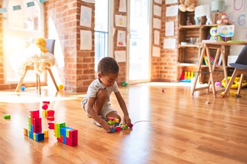 Beautiful african american toddler playing with wooden blocks train toy around lots of toys at kindergarten