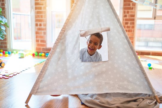 Beautiful african american toddler playing inside tipi smiling at kindergarten
