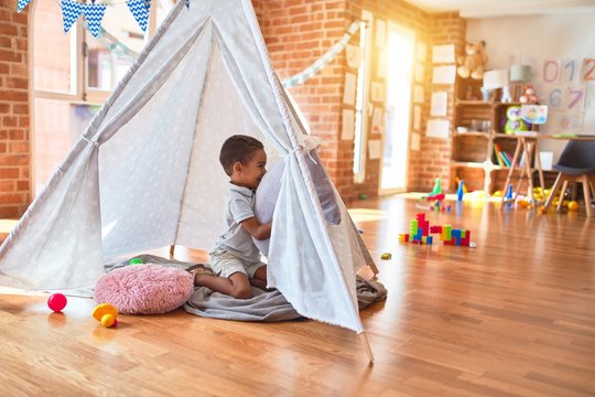 Beautiful african american toddler playing inside tipi smiling at kindergarten