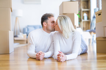 Young beautiful couple kissing lying down on the floor at new home around cardboard boxes