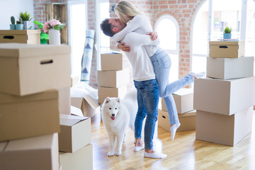 Fototapeta premium Young beautiful couple with dog hugging at new home around cardboard boxes